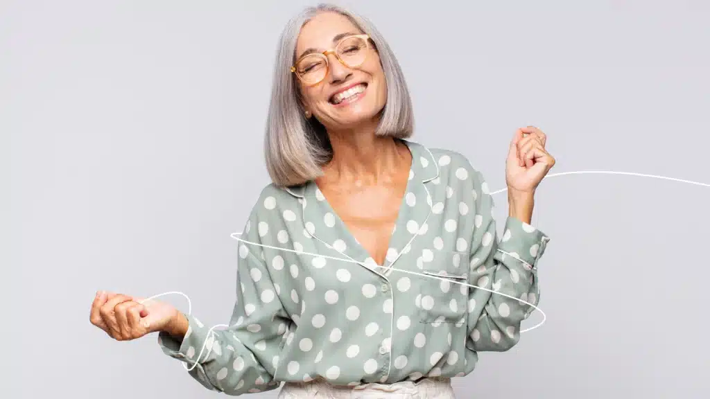 Femme âgée souriante en blouse à pois démêlant des écouteurs.