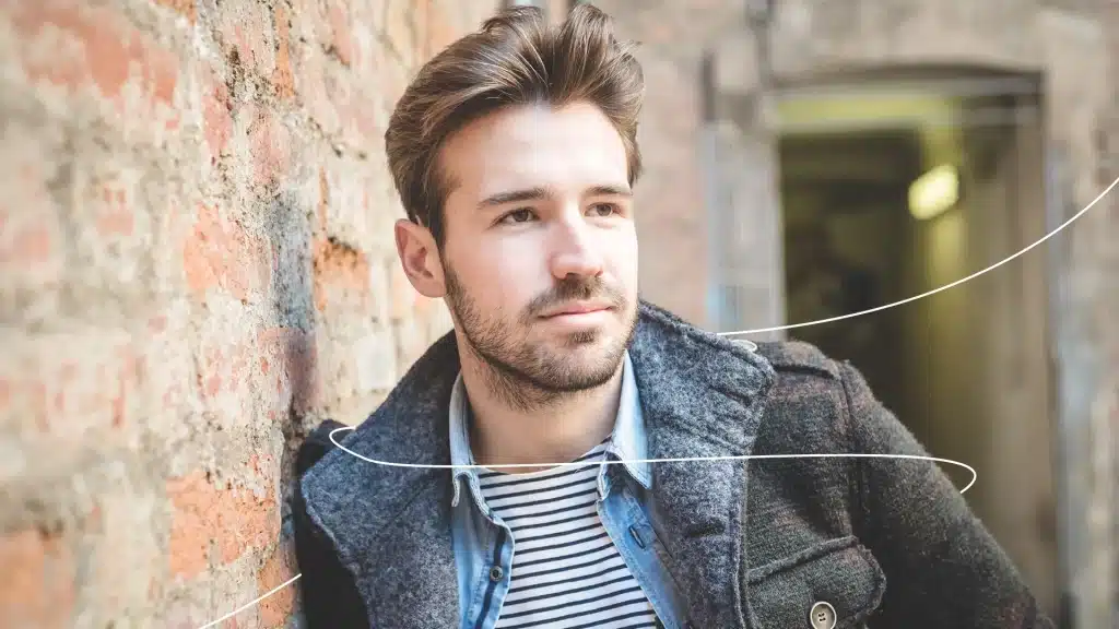 Man in coat leaning against brick wall.