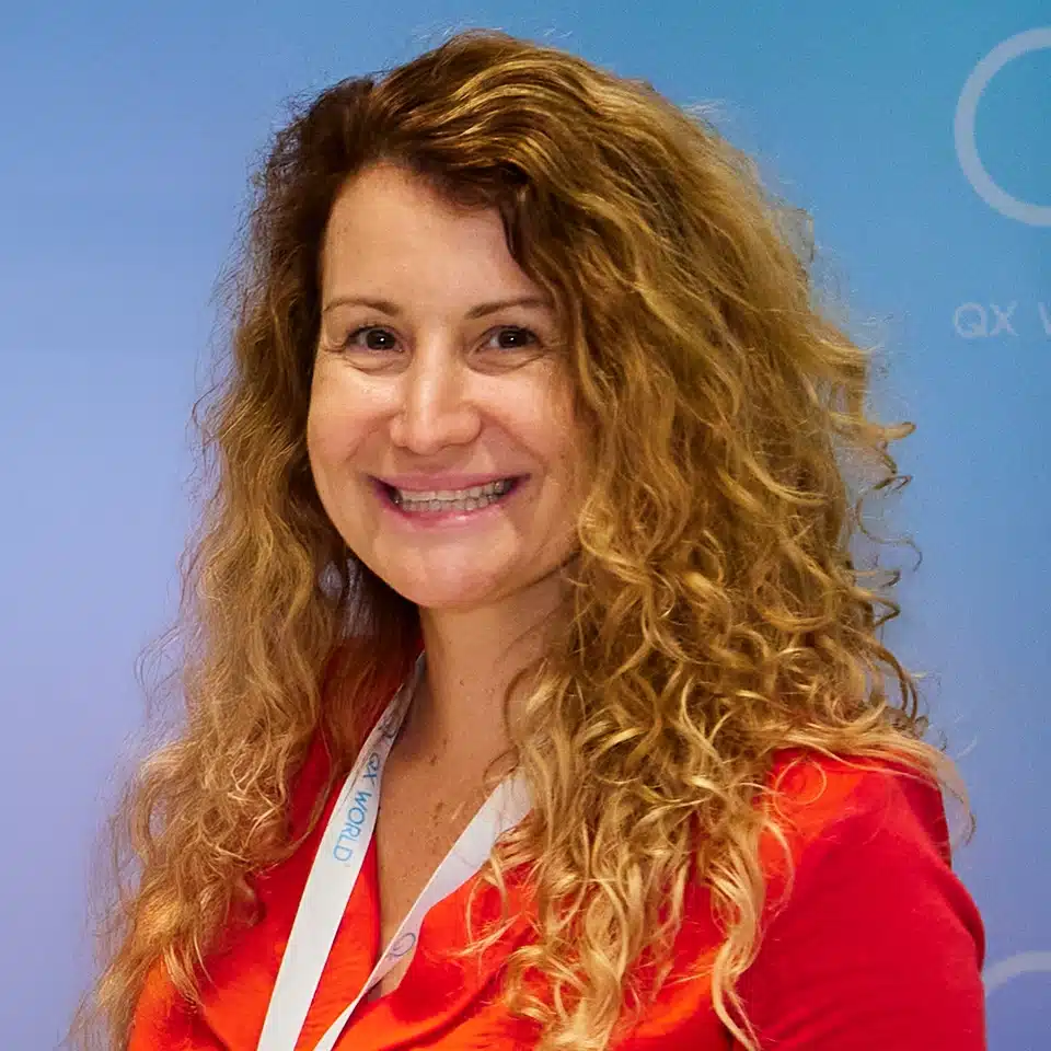 Femme souriante aux cheveux blonds bouclés portant un chemisier orange