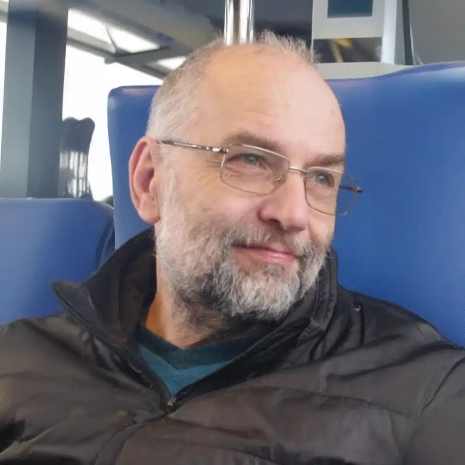 Homme âgé souriant avec des lunettes, assis dans un train